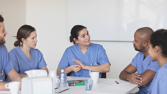 Pflegefachkräfte in medizinischer Arbeitskleidung sitzen an einem Tisch und tauschen sich in einer Besprechung aus.