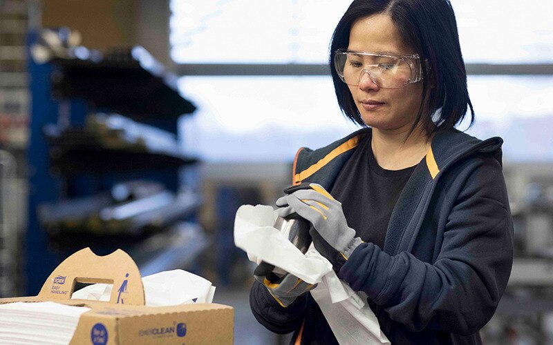 En kvinna i fabriksmiljö använder en Tork rengöringsduk och har en förpackning med Tork rengöringsdukar bredvid sig