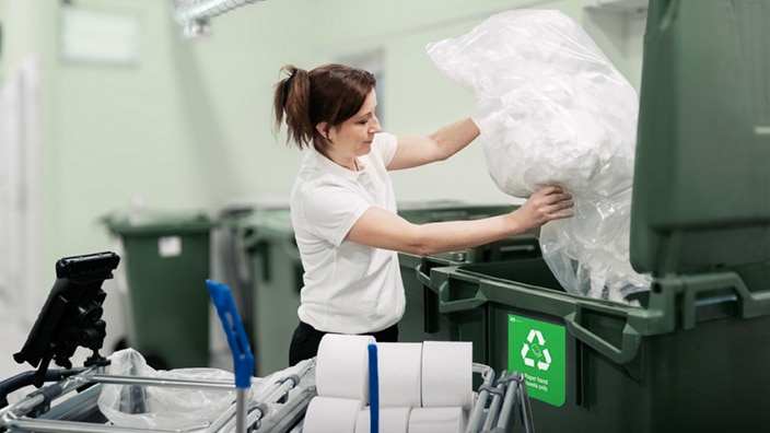 Die Reinigungskraft wirft die gesammelten gebrauchte Papierhandtücher in einen Behälter des Recyclingraums.