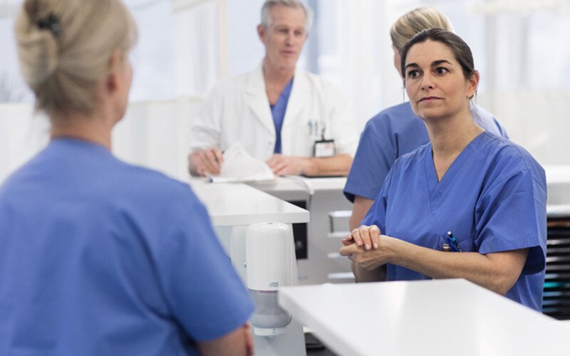 Verplegend personeel dat met elkaar praat, op de achtergrond een Tork Zeep en Handdesinfectie Dispenser en een arts die met een andere verpleger praat