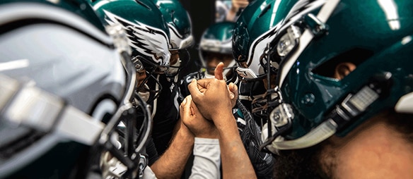 Philadelphia Eagles players huddle with hands joined, showing team unity before a game