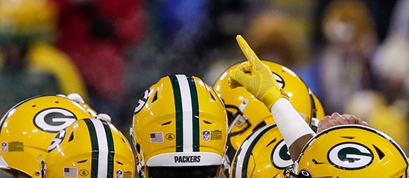Green Bay Packers players in yellow helmets, with one player raising a gloved hand and pointing upward."