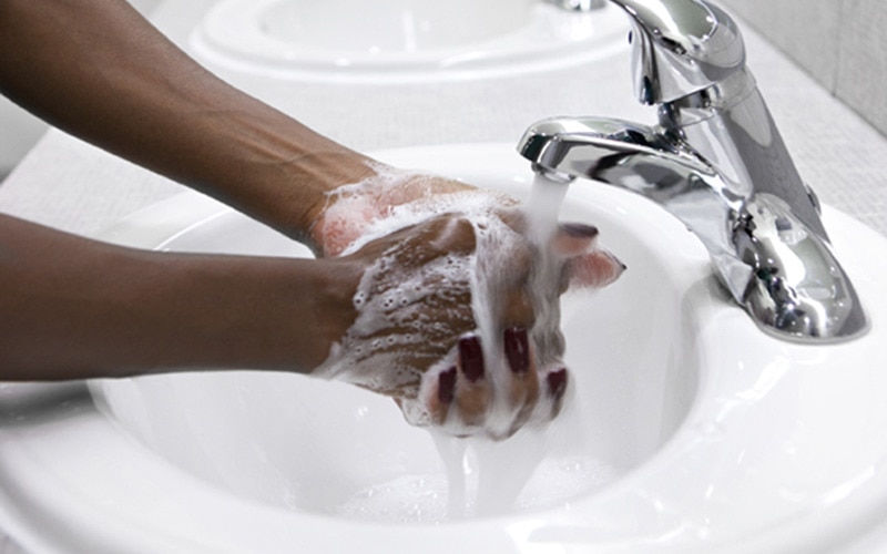Mani coperte di schiuma di sapone sotto un rubinetto aperto