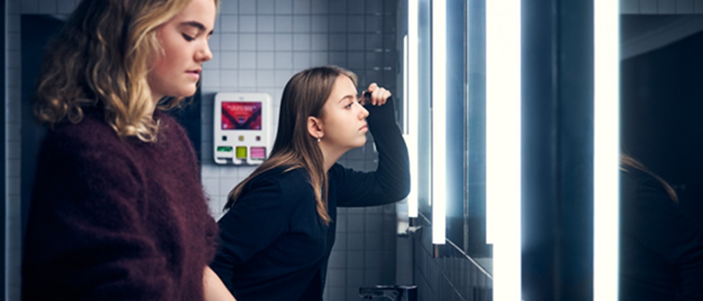 Moderne toiletruimte met dispenser en verlichte spiegel waar personen bij staan.