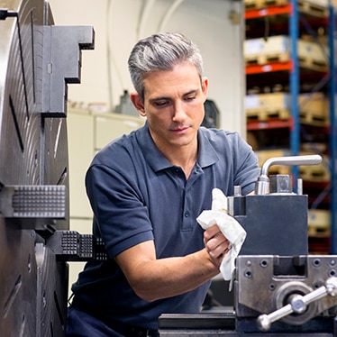 Person cleaning an industrial machine with a white cleaning cloth in a workshop