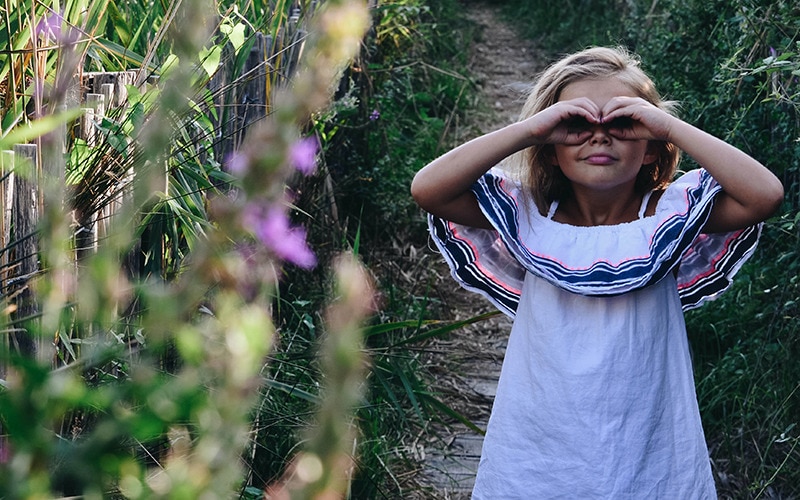 En flicka står intill ett fält och formar händerna till en kikare framför ögonen