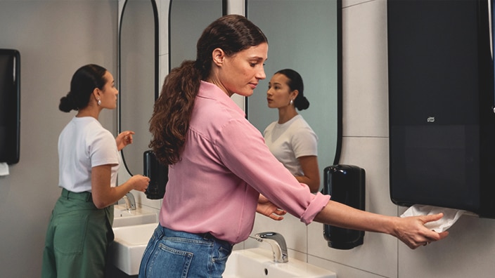 A person using a black Tork PeakServe dispenser A person using a black Tork PeakServe dispenser