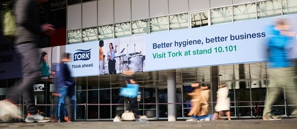 Banner op glazen gebouw met Tork-reclame en voorbijgangers