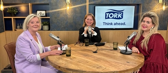 Drie personen aan een ronde tafel met microfoons in een podcaststudio, met een scherm met “Tork – Think ahead.” op de achtergrond.