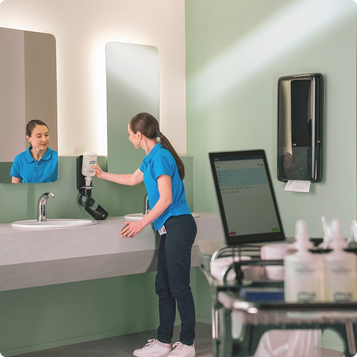Cleaner checking a soap dispenser after seeing a refill alert on the tablet app in the restroom 