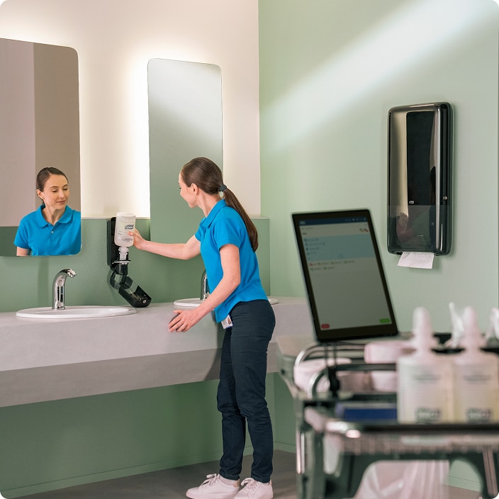 Cleaner checking a soap dispenser after seeing a refill alert on the tablet app in the restroom Cleaner checking a soap dispenser after seeing a refill alert on the tablet app in the restroom