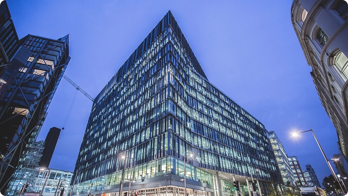 A modern glass office building illuminated at dusk.