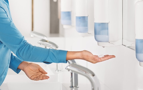 Osoba s rukou pod senzorem zásobníku na mýdla a dezinfekční prostředky