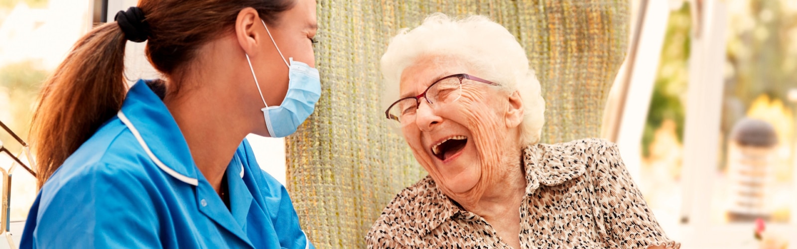 Een verpleegkundige en een oudere vrouw lachen