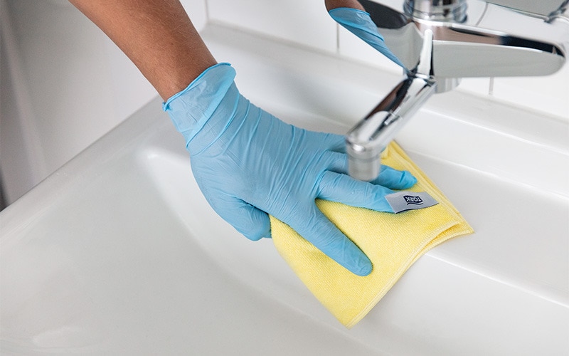 Gloved hand wipes sink with microfibre cloth