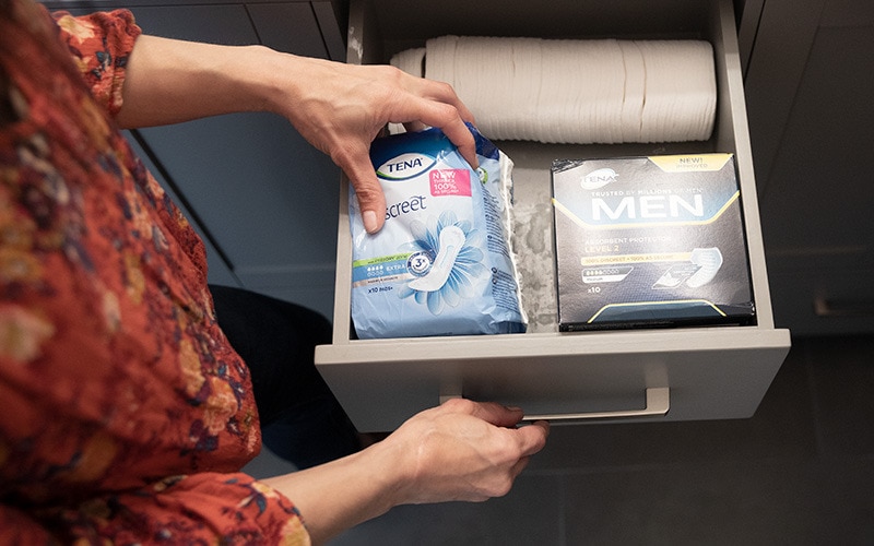 A person takes out a package of Tena pads from a drawer