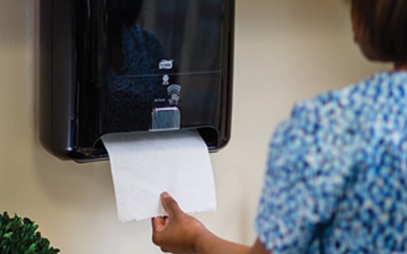 A person pulls a paper hand towel from a dispenser