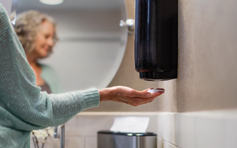 Les mains d’une femme couvertes de savon mousse placées en dessous d’un distributeur de savon