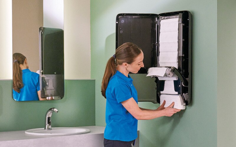 A cleaner refilling a hand towel dispenser.