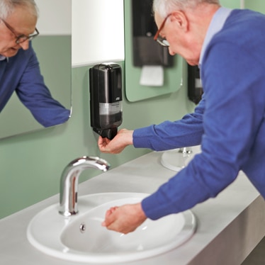 Older man washing his hands, taking soap from a dispenser