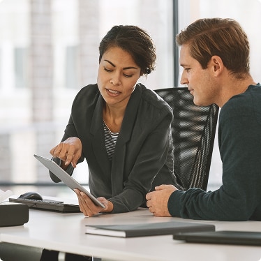 Two colleagues discussing information on a tablet in an office setting Two colleagues discussing information on a tablet in an office setting