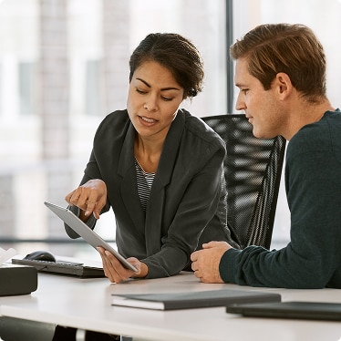 Two colleagues discussing information on a tablet in an office setting Two colleagues discussing information on a tablet in an office setting