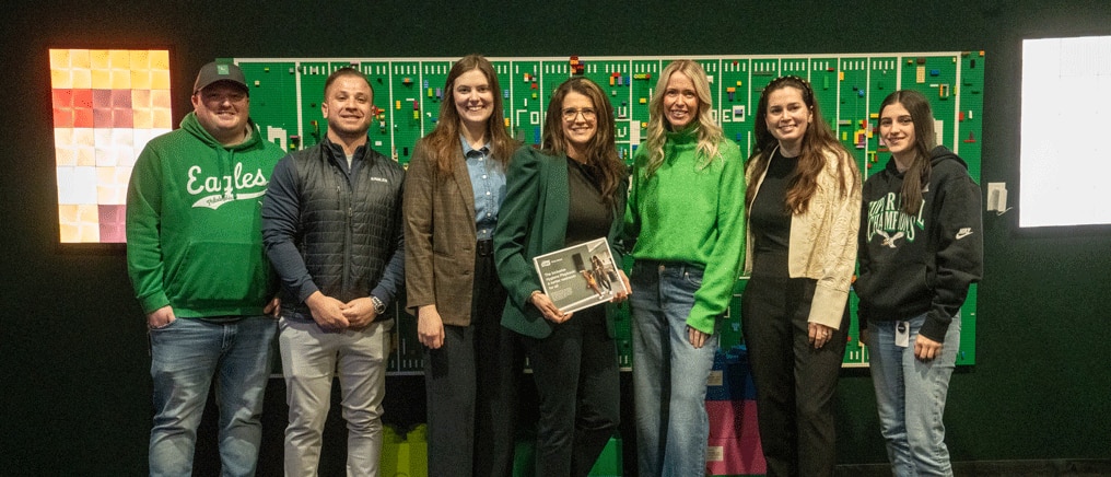 Tork and Eagles Autism Foundation representatives standing together in front of a green Eagles‑themed display wall. 