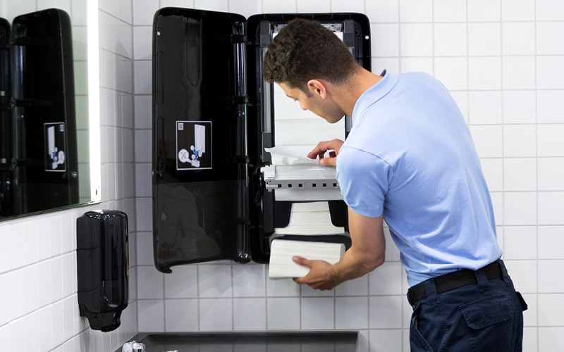 Limpiador reponiendo un dispensador de toallas de mano Tork PeakServe conectado al IdC