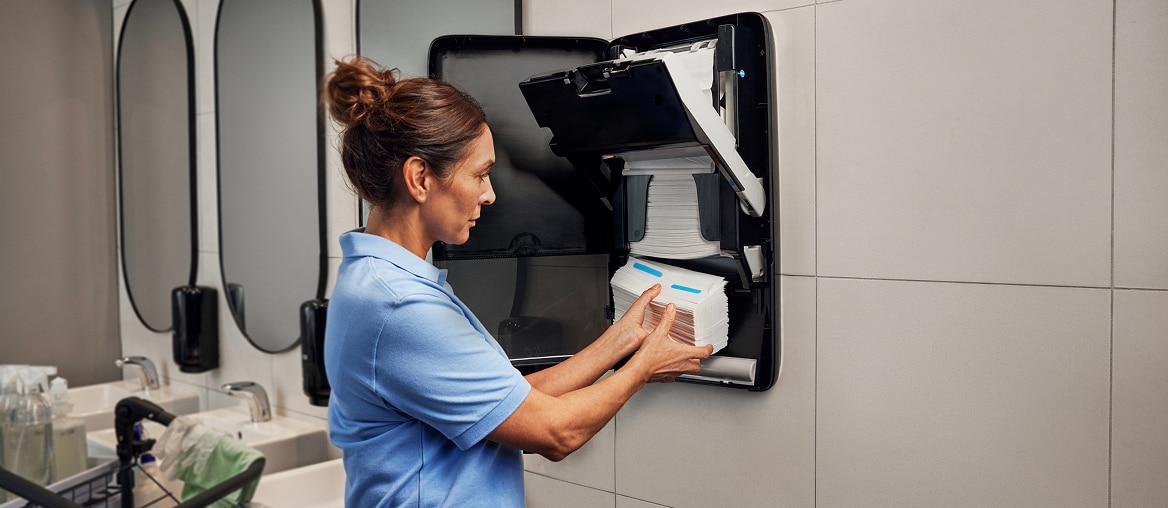 A cleaner loading towels into a black electronic hand towel dispenser
