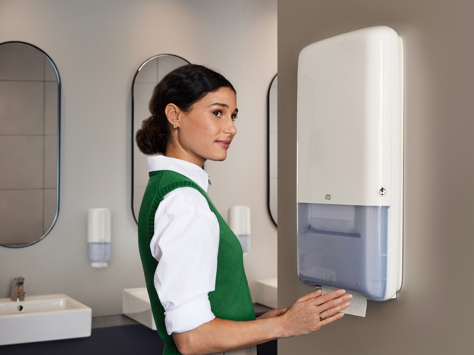 A person using a white Tork PeakServe Automatic hand towel dispenser in a washroom