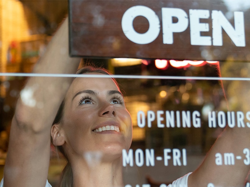 Woman putting up a sign in a window at a restaurant saying open