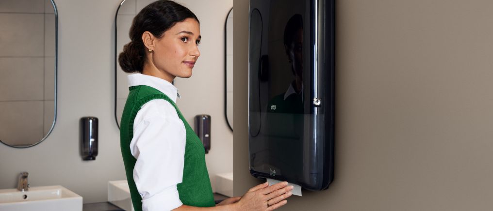 Person bruger PeakServe Automatic, en berøringsfri papirdispenser, ved en håndvask i et moderne badeværelse