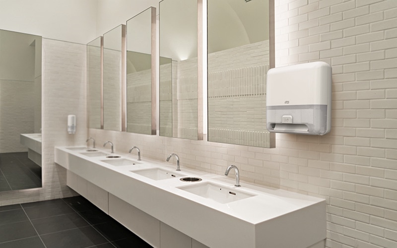 De sanitaire ruimte van een restaurant met witte Tork zeep- en handdoekdispensers