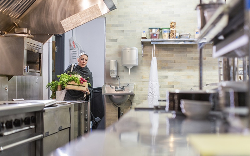 Woman in restaurant kitchen carrying produce