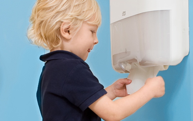 een jongen haalt een papieren handdoek uit een dispenser