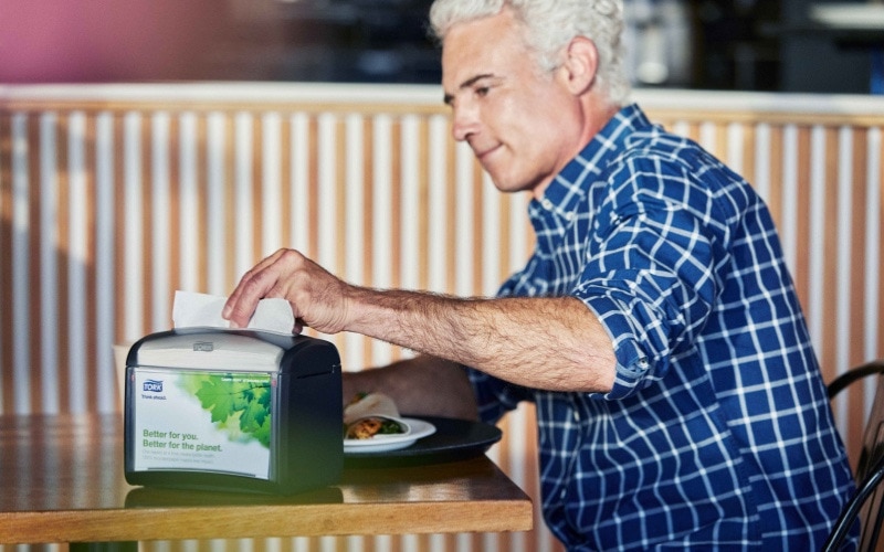 A man sitting at a table at a restaurant takes a napkin out of a dispenser 
