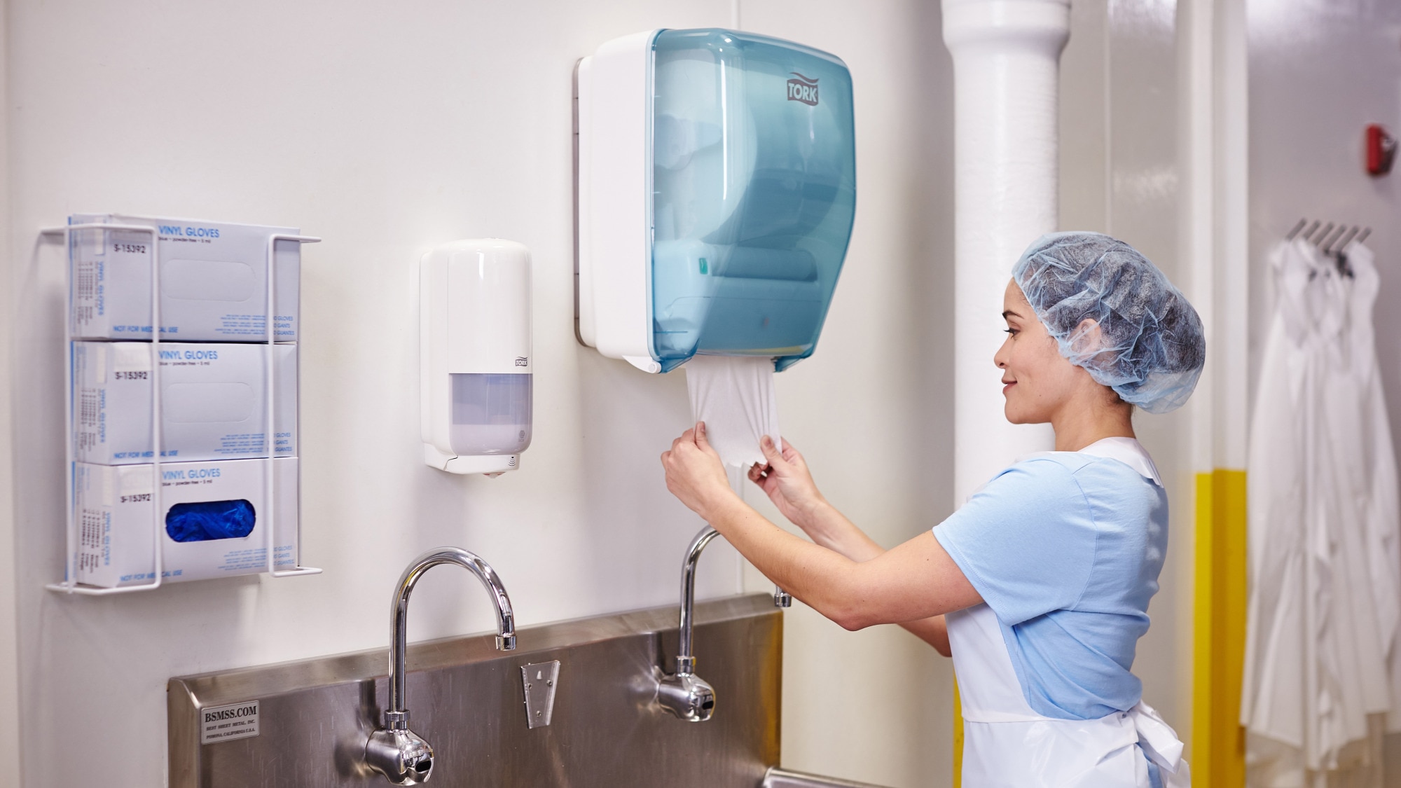 Woman in food processing wash area pulling paper towel from a Tork Washstation Dispenser. Woman in food processing wash area pulling paper towel from a Tork Washstation Dispenser.