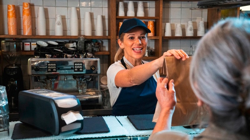 Une employée de restaurant remet un sac de nourriture à emporter à un client