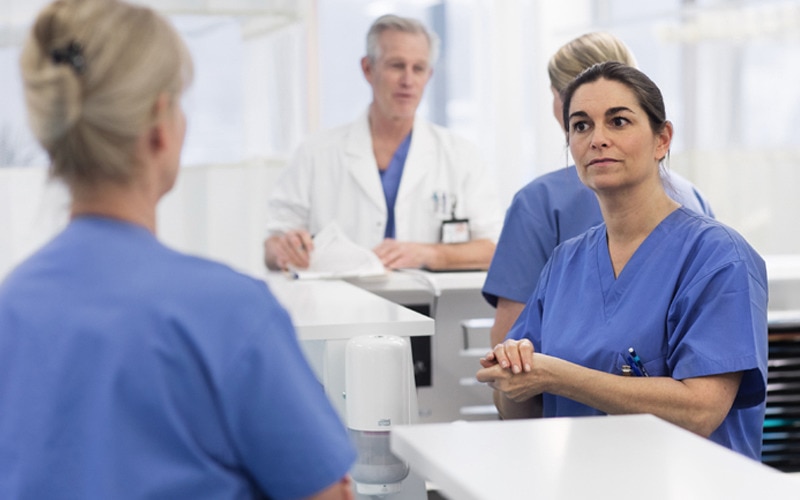 Två sjuksköterskor som pratar med varandra med en annan sjuksköterska och en läkare i bakgrunden