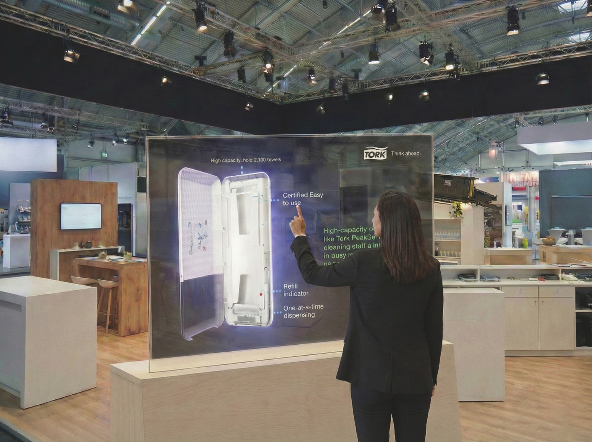 Woman at a trade show interacting with a digital touchscreen display featuring a Tork dispenser. Woman at a trade show interacting with a digital touchscreen display featuring a Tork dispenser.