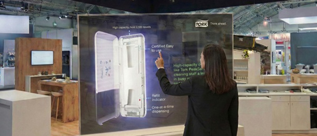 Frau auf einer Messe bedient einen digitalen Touchscreen mit einem Tork Spender