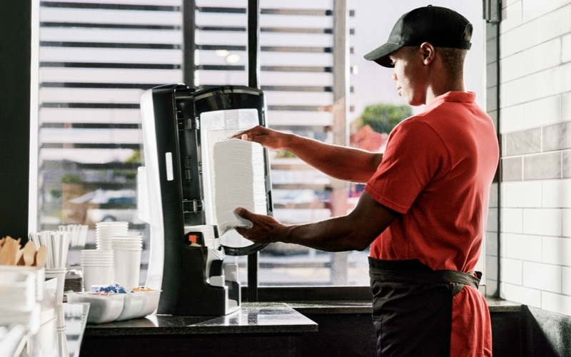 A man in an apron and cap refills a paper dispenser 