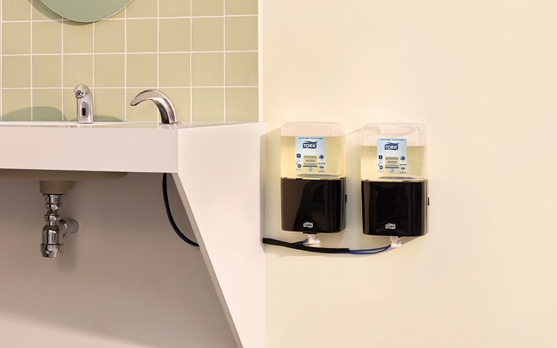 Close-up of two foam soap dispensers mounted on are restroom wall