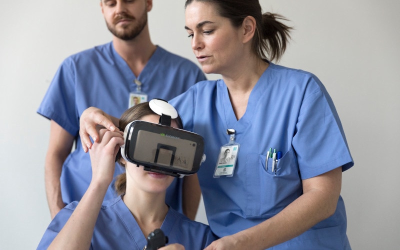 Three nurses and one of them is sitting down and wears virtual reality goggles