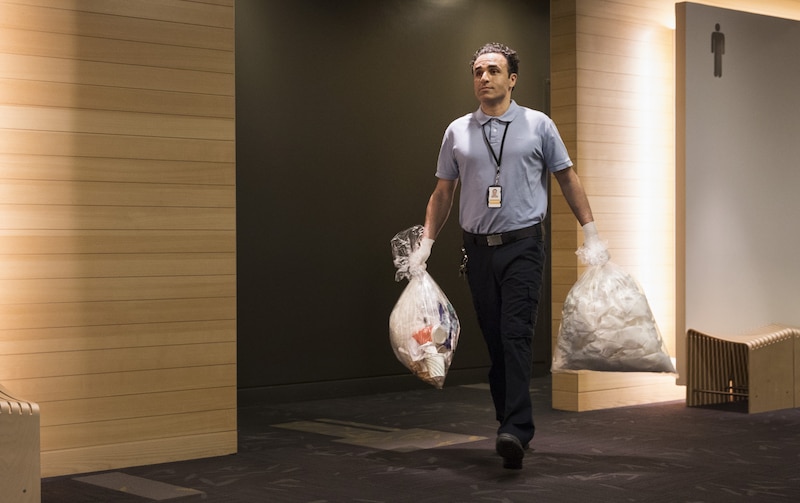 a man walking with plastic bags|a man walking with a bag of trash|a full bag of garbage|a bag of white paper|a blurry image of a person holding a cup|a man holding a bag of trash|a man wearing a badge|a light shining through a wood panel