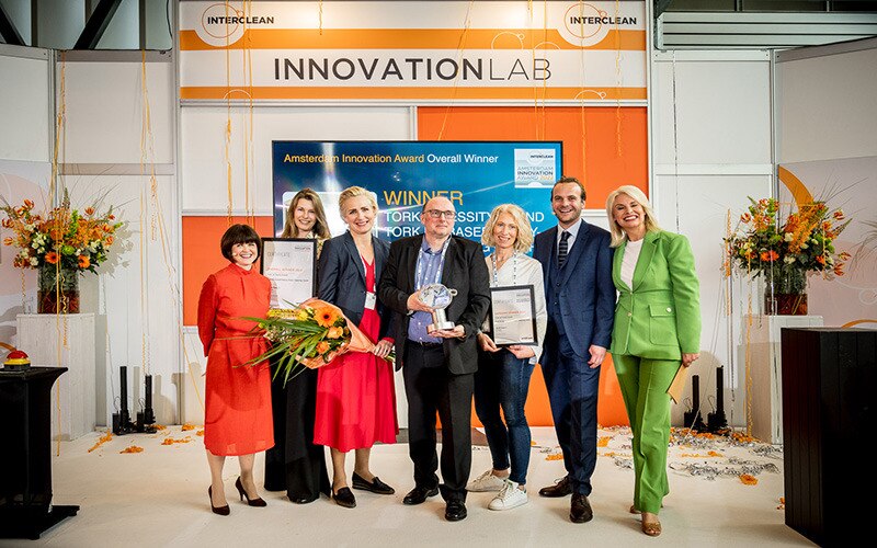 Gruppe von Personen, eine hält eine Preistrophäe, eine andere einen Blumenstrauß und zwei halten Diplome