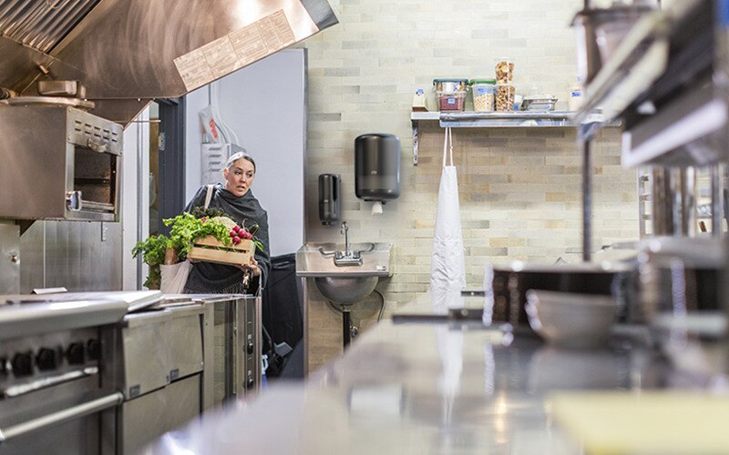 Woman in restaurant kitchen carrying produce