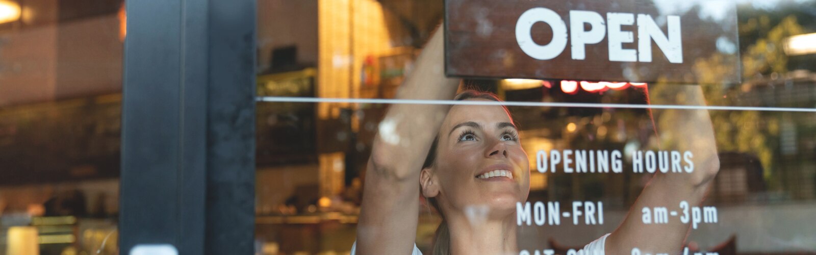 Vrouwen die enigszins omhoogkijken door een raam in een restaurant, met op het raam de gedeeltelijke openingstijden