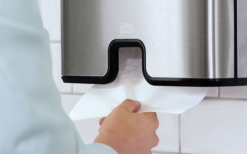Hand pulling a paper hand towel from a dispenser
