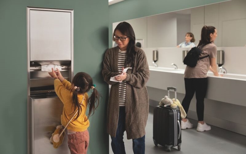 Child reaching for a paper hand towel in a washroom